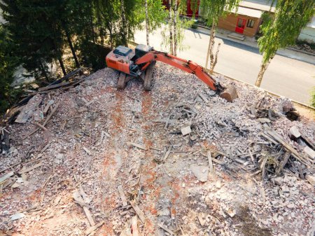 Téléchargez les photos : Vue aérienne de la démolition d'une vieille maison par une machine industrielle entourée d'arbres en été - en image libre de droit