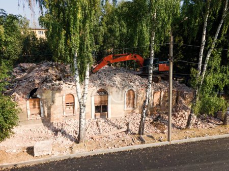 Téléchargez les photos : Véhicule moderne détruisant vieux bâtiment détérioré situé entre de grands arbres verts dans la campagne - en image libre de droit