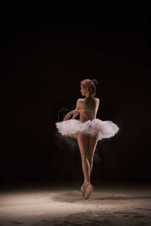 Téléchargez les photos : Jeune ballerine seins nus en jupe blanche debout en pointe dans un cours de danse sablonneuse - en image libre de droit