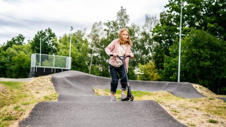 Téléchargez les photos : Preteen fille équitation scooter dans le parc. Enfant féminin mignon avec véhicule écologique à l'extérieur - en image libre de droit