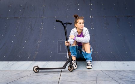 Foto de Linda chica sentada con scooter en la calle. Lindo adolescente posando con vehículo ecológico al aire libre - Imagen libre de derechos