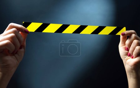 Photo for Hands holding yellow tape with black and yellow stripes on a dark background . Warning ribbon. - Royalty Free Image