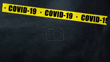 Téléchargez les photos : Ruban jaune avec texte COVID-19 sur fond sombre. Ruban d'avertissement. - en image libre de droit