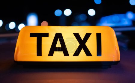 Téléchargez les photos : Taxi voiture jaune panneau lumineux sur la rue sombre la nuit avec éclairage. Symbole de service de cabine avec néon lumineux - en image libre de droit