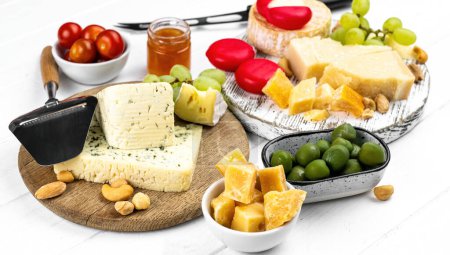 Foto de Diferentes tipos de queso servido con aceitunas verdes, tomate y uva para una nutrición gourmet. Parmesano ecológico y brie con delicatessen miel - Imagen libre de derechos
