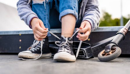 Foto de Girl sitting with scooter and tying shoelaces on sneakers. Person shoes and eco vehicle closeup - Imagen libre de derechos