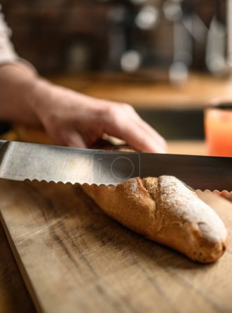 Photo for Girl hand cut french baguette with knife at kitchen. Tasty rustic fresh bread from for breakfast meal - Royalty Free Image