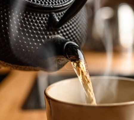 Téléchargez les photos : Verser le thé noir chaud de théière en métal à la cuisine fermer. La vapeur sort de la tasse. Traditions de consommation de thé. - en image libre de droit
