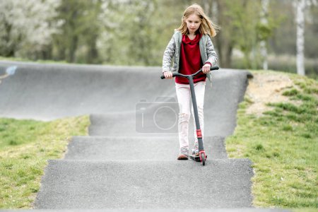 Téléchargez les photos : Beautiful little girl rides a scooter in a extreme ride park - en image libre de droit