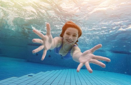 Téléchargez les photos : Teen girl swimming under water in blue pool and posing looking at camera. Pretty female teenager diving and enjoying summer activity - en image libre de droit