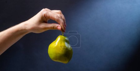 Foto de Mano sosteniendo pera verde sobre fondo azul. Fruta fresca natural ecológica para una dieta vegana saludable en vitaminas - Imagen libre de derechos