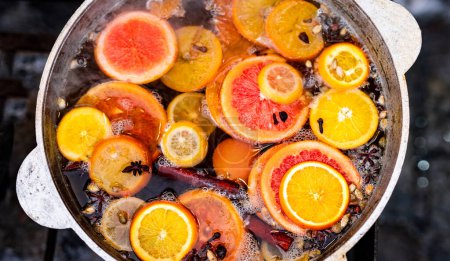 Téléchargez les photos : Vigne épicée cuite avec des oranges en pot dans le marché de la nourriture de rue. Boisson alcoolisée chaude colorée au festival de foire en plein air gros plan - en image libre de droit