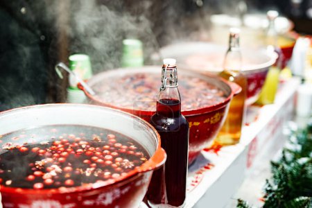 Téléchargez les photos : Boissons baies chaud vin chaud chaud dans des pots dans le marché de la nourriture de rue à la période de Noël. Boissons chaudes festives colorées au festival de Noël en plein air close seup - en image libre de droit