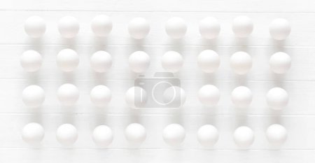 Téléchargez les photos : Oeufs blancs crus rangées sur une table en bois blanc vue d'en haut - en image libre de droit