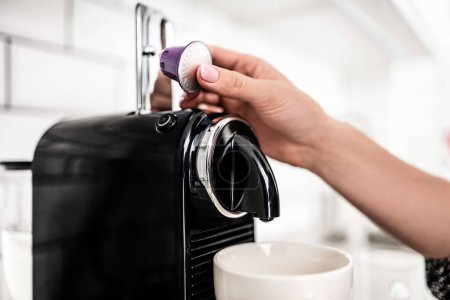 Foto de Girl hand put capsule to coffee machine at home closeup. Woman preparing italian caffeine beverage using professional espresso maker - Imagen libre de derechos