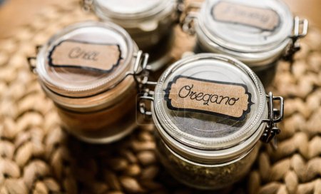 Photo for Set of different spicies in glass jars at the kitchen. Black pepper and dried greens. - Royalty Free Image