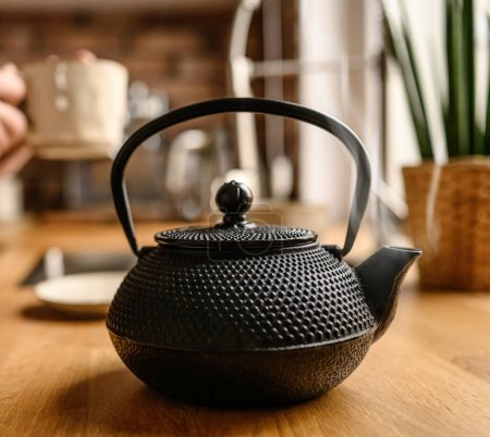 Foto de Tetera de metal negro con té caliente en la cocina. El vapor viene del caño del té. Tradiciones de té. Chica haciendo un té. - Imagen libre de derechos