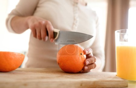 Téléchargez les photos : Femme coupée orange mûr avec couteau pour faire du jus naturel à la cuisine. Guy main préparant boisson aux fruits tropicaux à partir d'agrumes - en image libre de droit