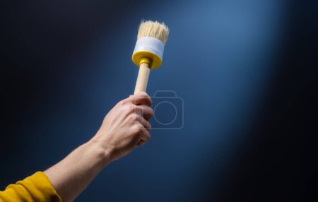 Photo for Hand holding brush for interior renovation up on blue background. Person with paintbrush decoration tool preparing for craft home improvement - Royalty Free Image