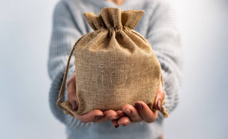 Photo for Person holding burlap bag in hands with gift inside. Girl with rustic beige pouch packaging made with organic textile - Royalty Free Image