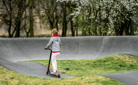 Photo for Beautiful little girl rides a scooter in a extreme ride park, back view - Royalty Free Image