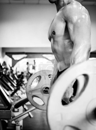 Foto de Musculoso culturista de pie con un peso de barbo en un moderno gimnasio listo para hacer ejercicios - Imagen libre de derechos
