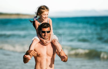 Foto de Padre sosteniendo a su hija a hombros en los retratos de la costa. Padre de familia y pequeño niño bonito en la playa en verano juntos - Imagen libre de derechos