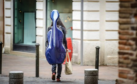 Photo for Girl carries a cello in a blue trunk by the quiet European Street - Royalty Free Image