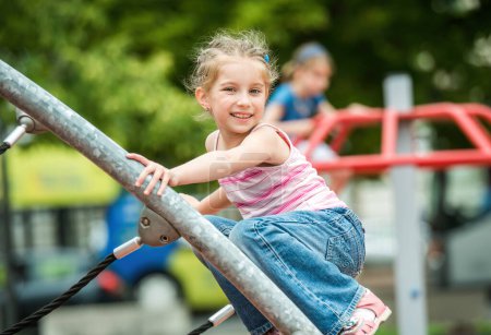 Téléchargez les photos : Joyeux mignon petite fille jouer à l'aire de jeux en plein air - en image libre de droit