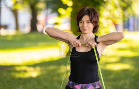 Photo for Girl with rubber elastic band doing arm resistance workout outdoors in park. Young woman exercising at morning with additional equipment - Royalty Free Image
