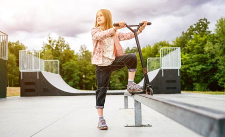 Photo for Preteen girl standing with scooter on ramp in the park. Cute child posing with eco vehicle outdoors - Royalty Free Image