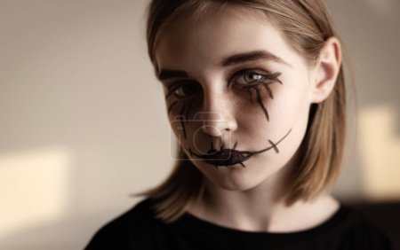Téléchargez les photos : Petite fille avec le maquillage effrayant Halloween yeux brossés regardant la caméra. Portrait effrayant d'enfants avec l'expression folle de plaisantin. - en image libre de droit