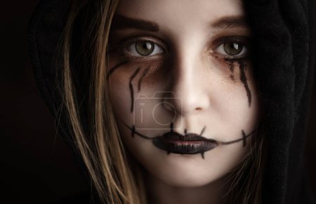 Téléchargez les photos : Petite fille avec le maquillage effrayant d'Halloween regardant le portrait de gros plan de caméra. Enfant effrayant avec une expression folle de blagueur. - en image libre de droit