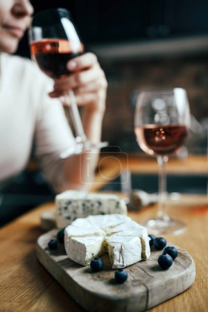 Foto de Plato de queso brie francés en una mesa con mujeres bebiendo un vino de rosas sobre un fondo borroso en la cocina - Imagen libre de derechos