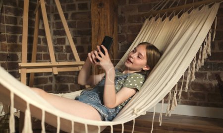 Photo for Preteen child girl lying in hammock in loft room at home. Pretty female kid enjoying summer vacation - Royalty Free Image