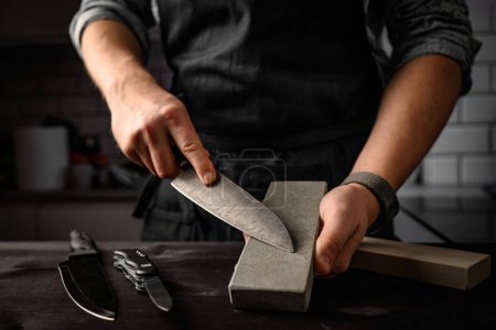 Foto de Hombre afilando un cuchillo con afilar herramienta de piedra. Cuchillo afilador maestro en una piedra de afilar - Imagen libre de derechos