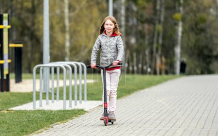 Photo for Little cute girl riding a scooter on a path in the park - Royalty Free Image