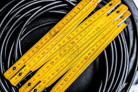 Foto de Herramienta de regla amarilla en cable de cuerda negro para medir objetos con precisión. Instrumento de equipo de centímetro de trabajo para precisión de longitud - Imagen libre de derechos