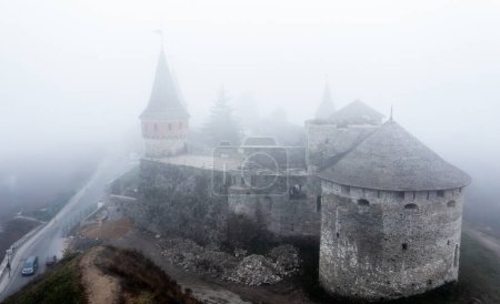 Téléchargez les photos : Ancienne forteresse à Kamenets-podolsky, Ukraine par temps brumeux de vue aérienne. Ancien château médiéval avec des tours dans les nuages du drone - en image libre de droit