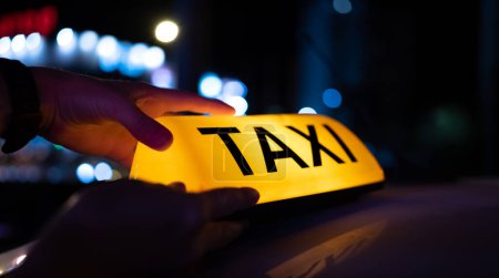 Téléchargez les photos : Lumière de voiture de taxi sur la rue sombre de la ville la nuit. Panneau au néon de la cabine sur le toit du véhicule qui brille au crépuscule le soir - en image libre de droit