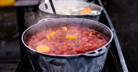 Téléchargez les photos : Boissons fraise et orange chaud vin chaud chaud dans des pots dans le marché de la nourriture de rue. Boissons chaudes aux fruits colorés au festival de foire en plein air gros plan - en image libre de droit