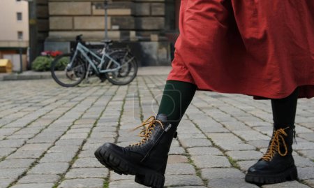 Chica en falda roja camina por parte histórica de la ciudad europea, piernas vestidas con botas negras