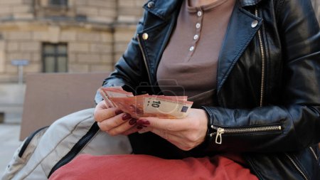 Téléchargez les photos : Attrayant femme compte Euro Cash sur le banc de rue de la ville - en image libre de droit