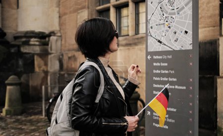 Téléchargez les photos : Attractive Promenades Touristiques Féminines Avec L'Allemagne Drapeau Dans Le Centre Historique De Dresde, Vérification De L'itinéraire Touristique Sur La Carte De La Ville - en image libre de droit