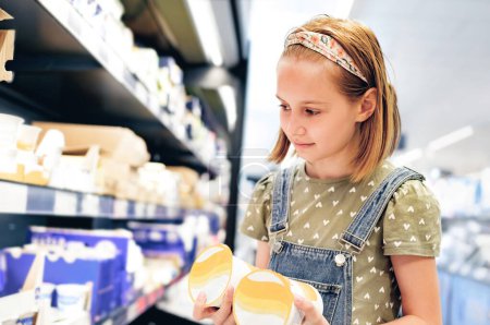 Photo for Pretty girl child choosing yogurt in supermarket shop. Beautiful female preteen kid looking milk products in grocery store - Royalty Free Image