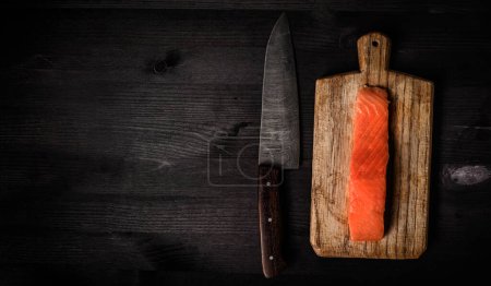 Téléchargez les photos : Filet de poisson rouge saumon cru sur une planche à découper avec un grand couteau de cuisine, vue du dessus avec un espace de copie - en image libre de droit