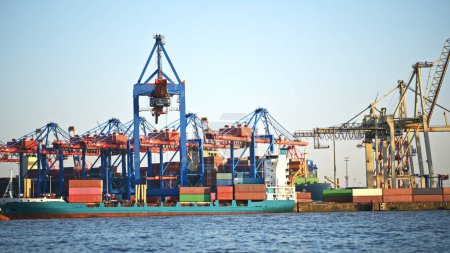 Téléchargez les photos : Grue de fret dans le port maritime avec des conteneurs pour l'importation et l'exportation d'expédition à Hambourg. Quai commercial portuaire avec équipement pour la livraison globale de marchandises logistiques - en image libre de droit