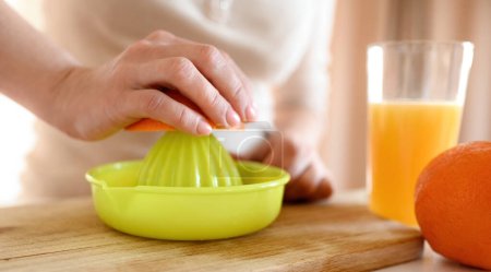 Téléchargez les photos : Fille main serrer orange mûr avec extracteur manuel pour faire du jus naturel à la cuisine. Femme préparant boisson aux fruits tropicaux - en image libre de droit