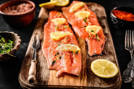 Foto de Trucha de pescado rojo con limón y especias listas para cocinar en una tabla de cortar. Comida saludable y buena fuente de ácido Omega-3 y vitaminas. - Imagen libre de derechos