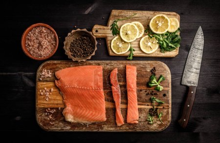 Téléchargez les photos : Filet de poisson rouge saumon aux herbes et citron prêt pour cuisiner un dîner sain sur une table noire, vue sur le dessus - en image libre de droit